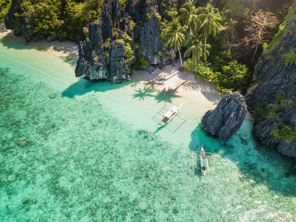 Boats anchored beside a sandy beach and limestone cliffs in the El Nido area